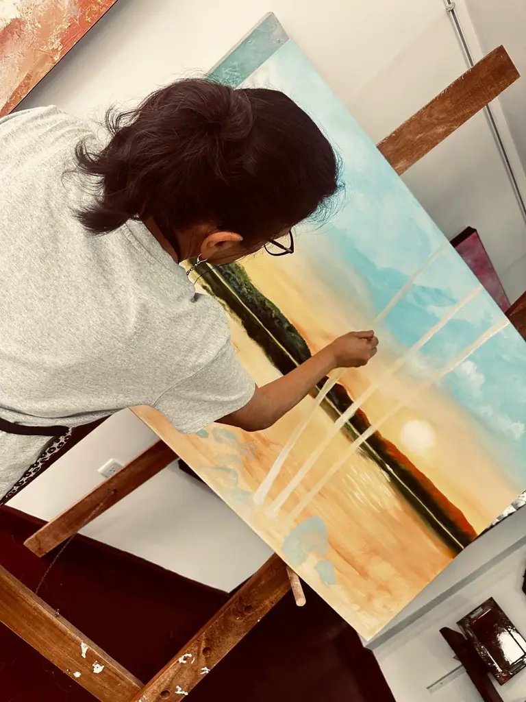 Estudiante pintando al óleo un paisaje de atardecer sobre un caballete.