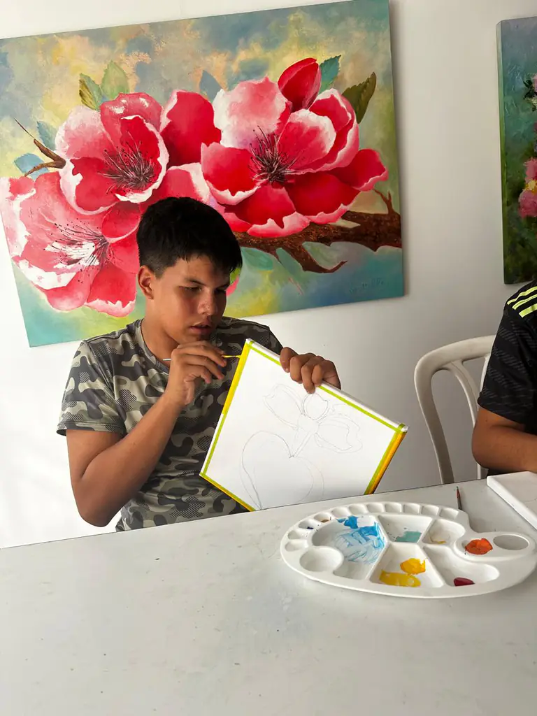 Estudiante adolescente muestra el boceto a lápiz de una flor sobre su lienzo.